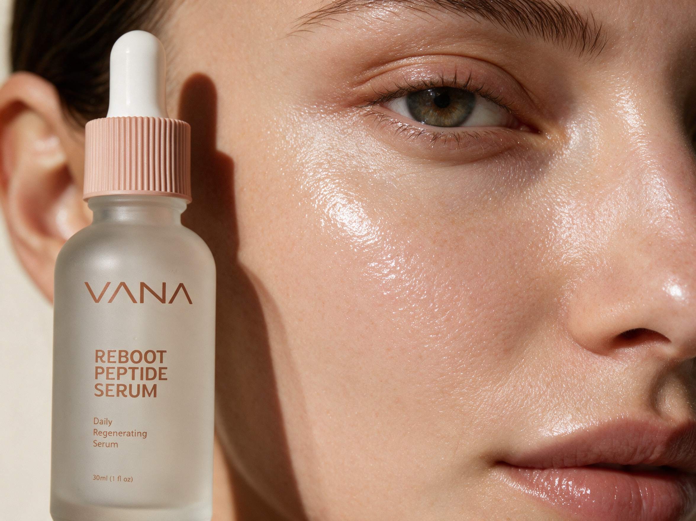Close-up of glowing hydrated skin beside the VANA Reboot Peptide Serum bottle